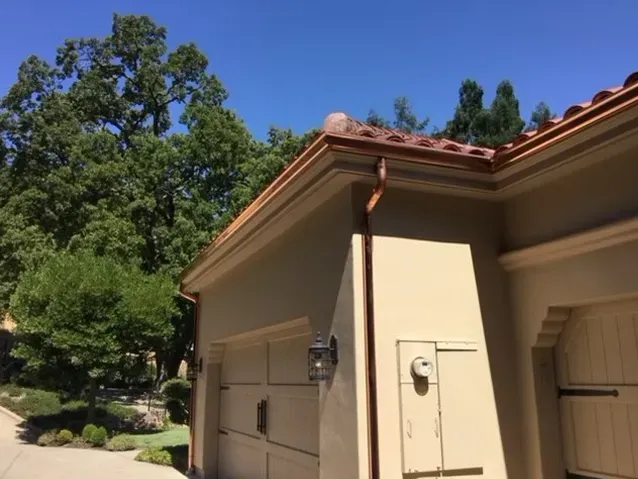 Copper gutter and downspout along the edge of a stucco home with a tile roof.